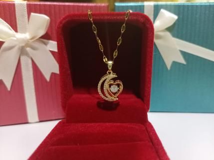 Collar de oro con colgante de luna y corazón en un joyero de terciopelo rojo, con cajas de regalo envueltas en el fondo.