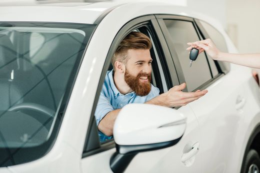 Un uomo in un'auto bianca riceve le chiavi, sorridendo.