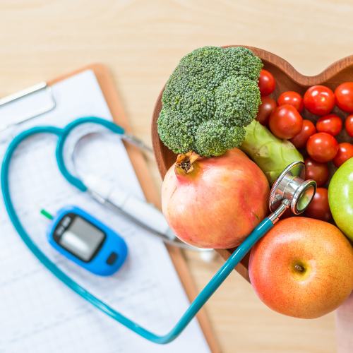 Heart-shaped bowl of fruit with stethoscope, glucose monitor, and clipboard, symbolizing healthy diet for diabetes care.
