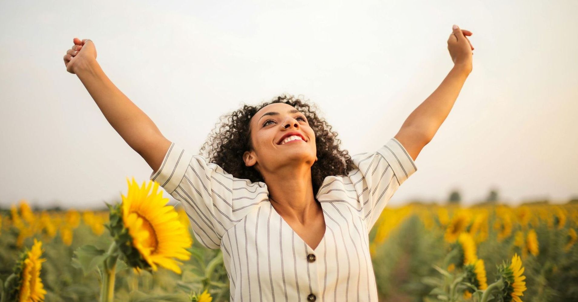 Woman in sunflower field with her arms stretched wide and smiling. 