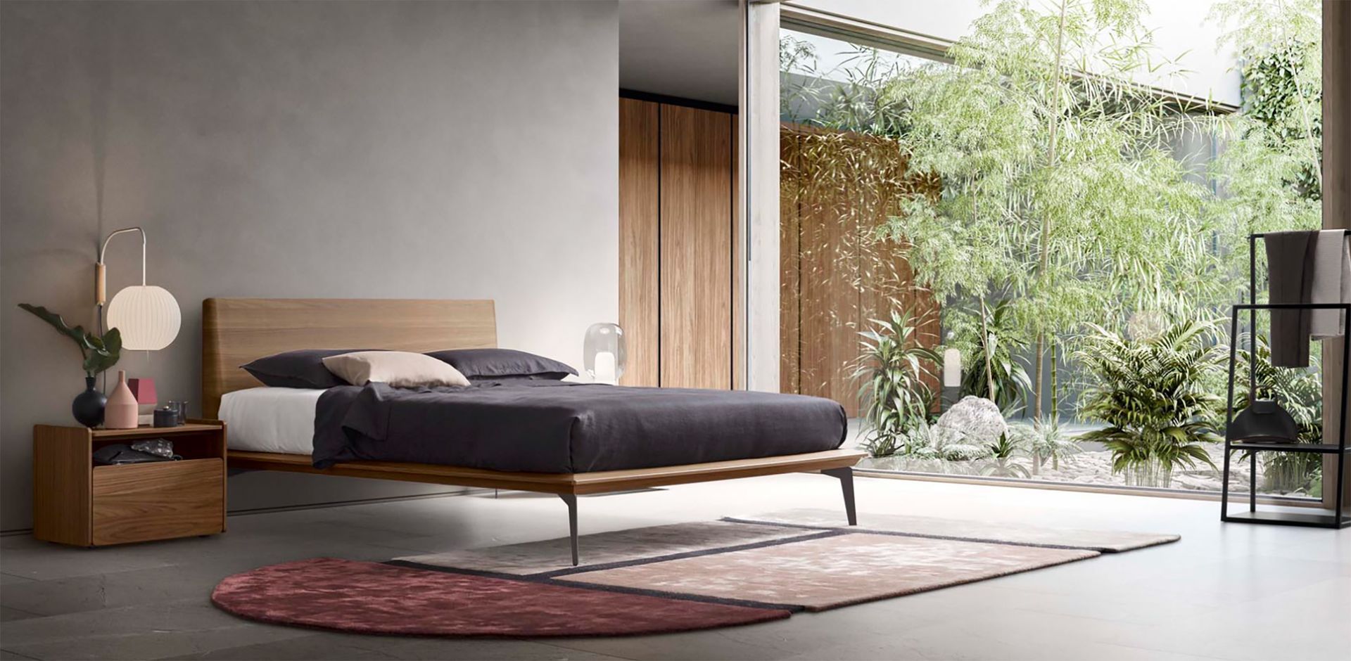 Camera da letto moderna con letto basso in legno, pareti grigie e un'ampia finestra che si affaccia sul verde.