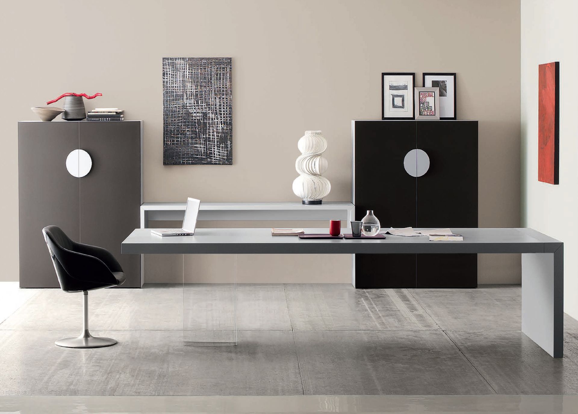 Ufficio moderno con scrivania grigia, sedia nera, armadietti, opere d'arte e decorazioni contro una parete neutra.