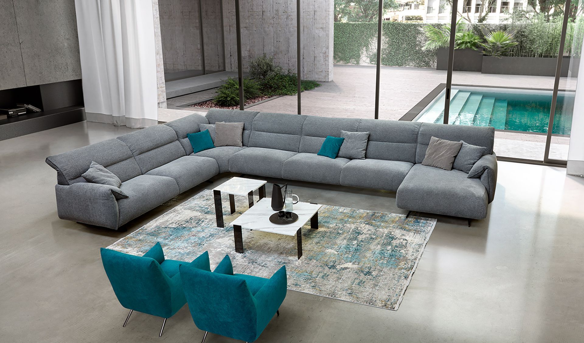 Soggiorno moderno con divano componibile grigio, sedie turchesi e vista sulla piscina attraverso pareti di vetro.