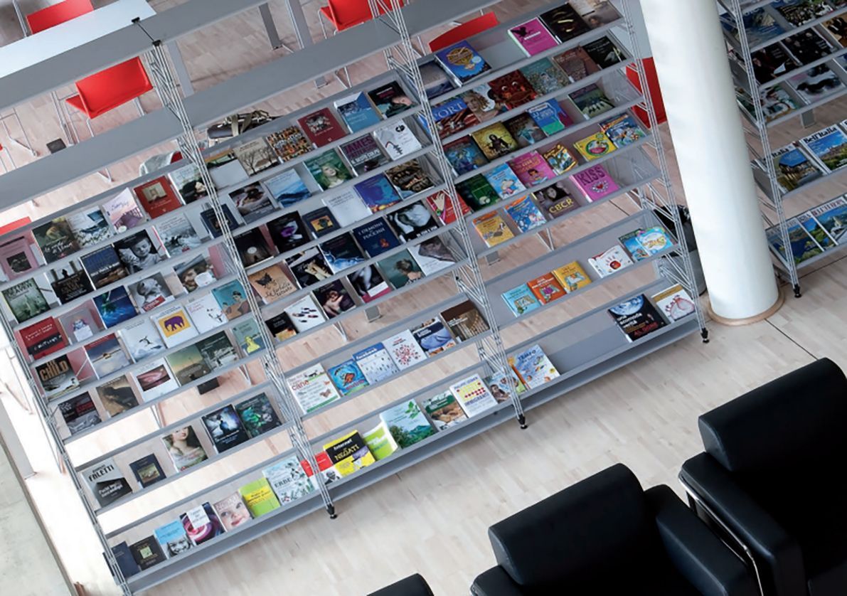 Vista dall'alto di una biblioteca. Scaffali pieni di libri, poltrone nere e una colonna bianca.