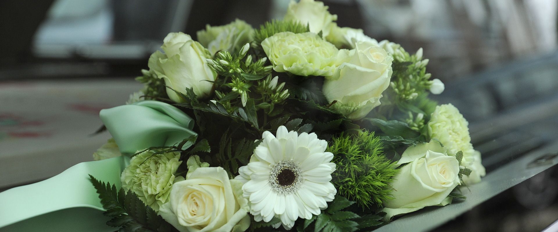Close-up of white flowers, including roses and daisies, with green accents and ribbon.