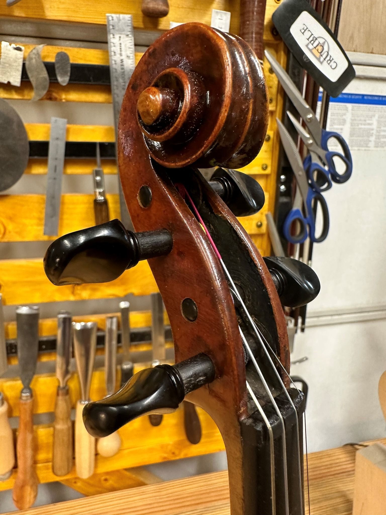 A violin is sitting on a table in front of a wall of tools