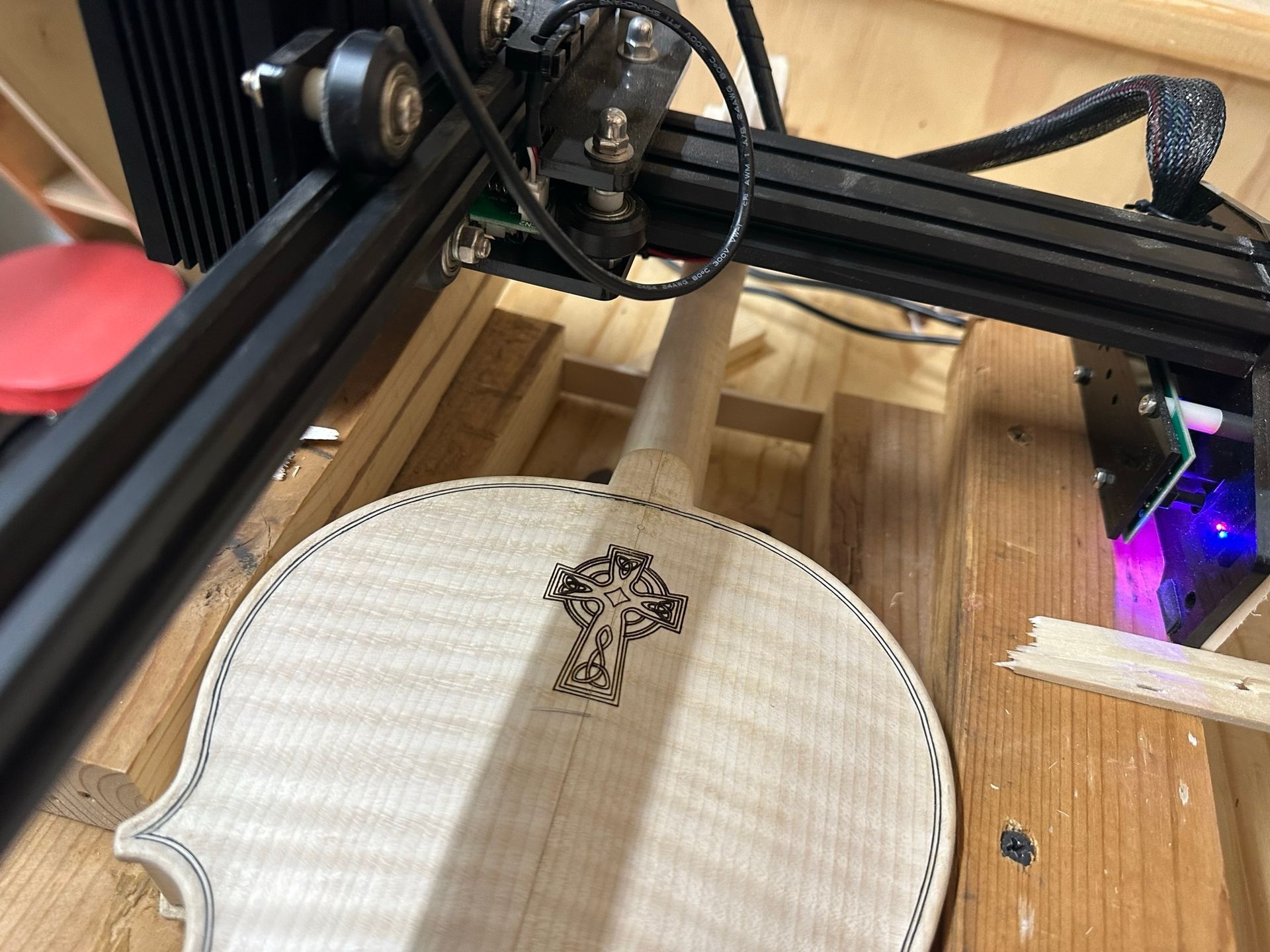A violin is being engraved by a machine on a wooden table
