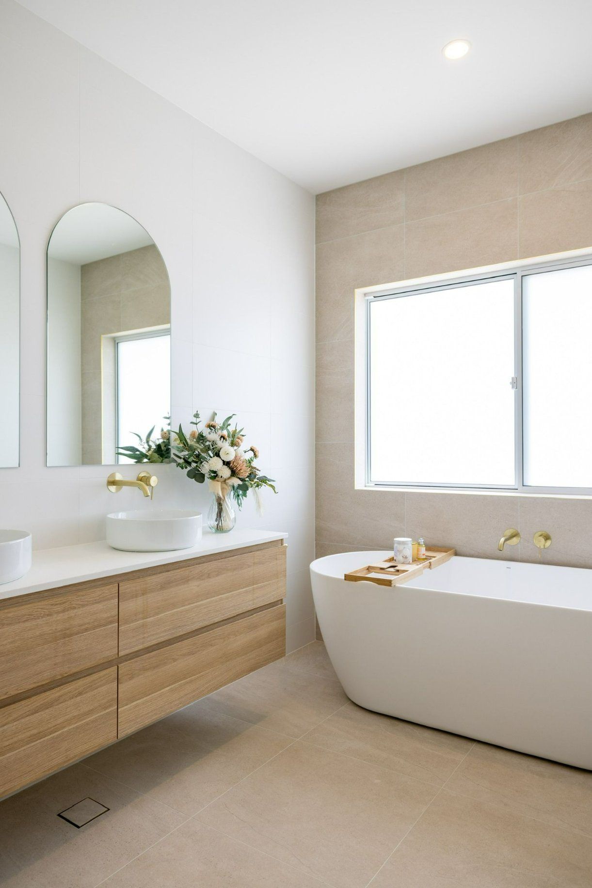 Modern bathroom with a white tub, wood vanity, and arched mirrors. — Blue Horizon Projects in Bateau Bay, NSW