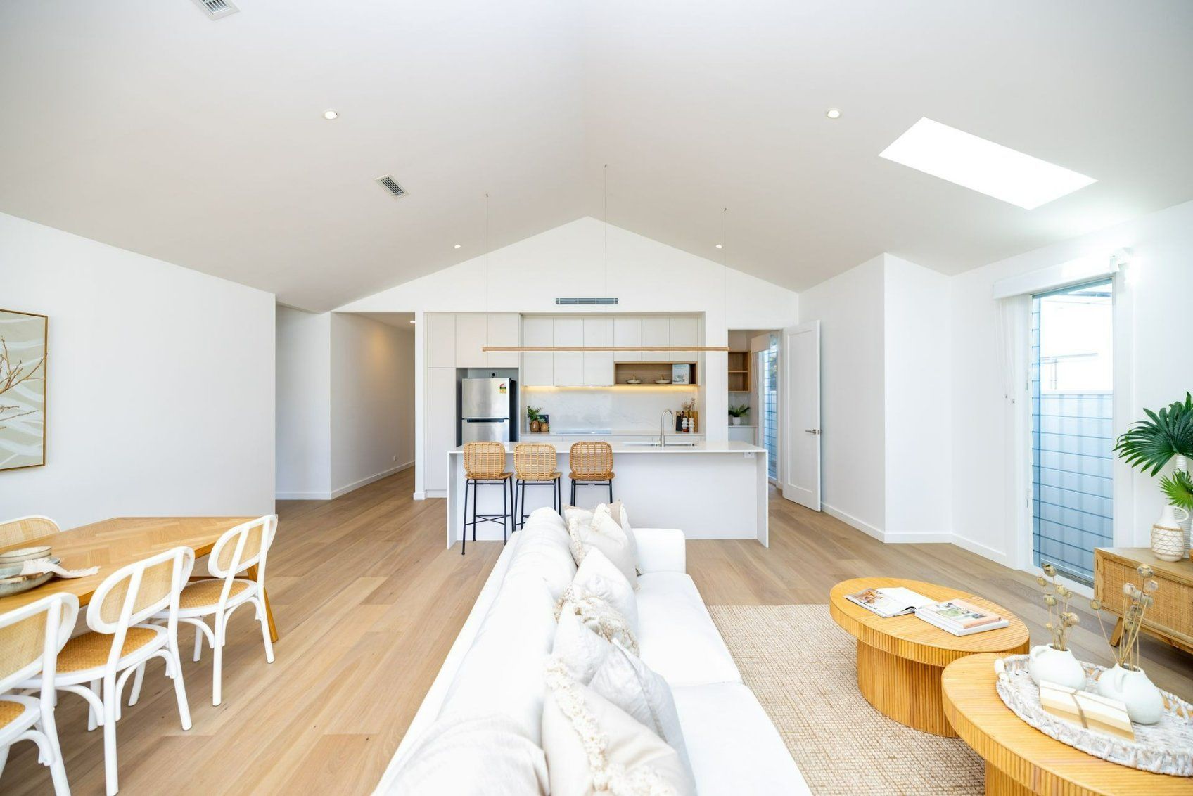 Bright, open-plan living area with kitchen, dining, and living room. White walls, light wood floors, and modern decor. — Blue Horizon Projects in Bateau Bay, NSW