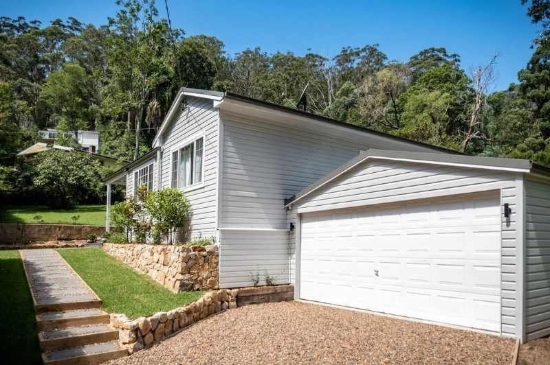 A Modern White Home with A Garage, Nestled Among Lush Greenery and Trees — Blue Horizon Projects in Bateau Bay, NSW