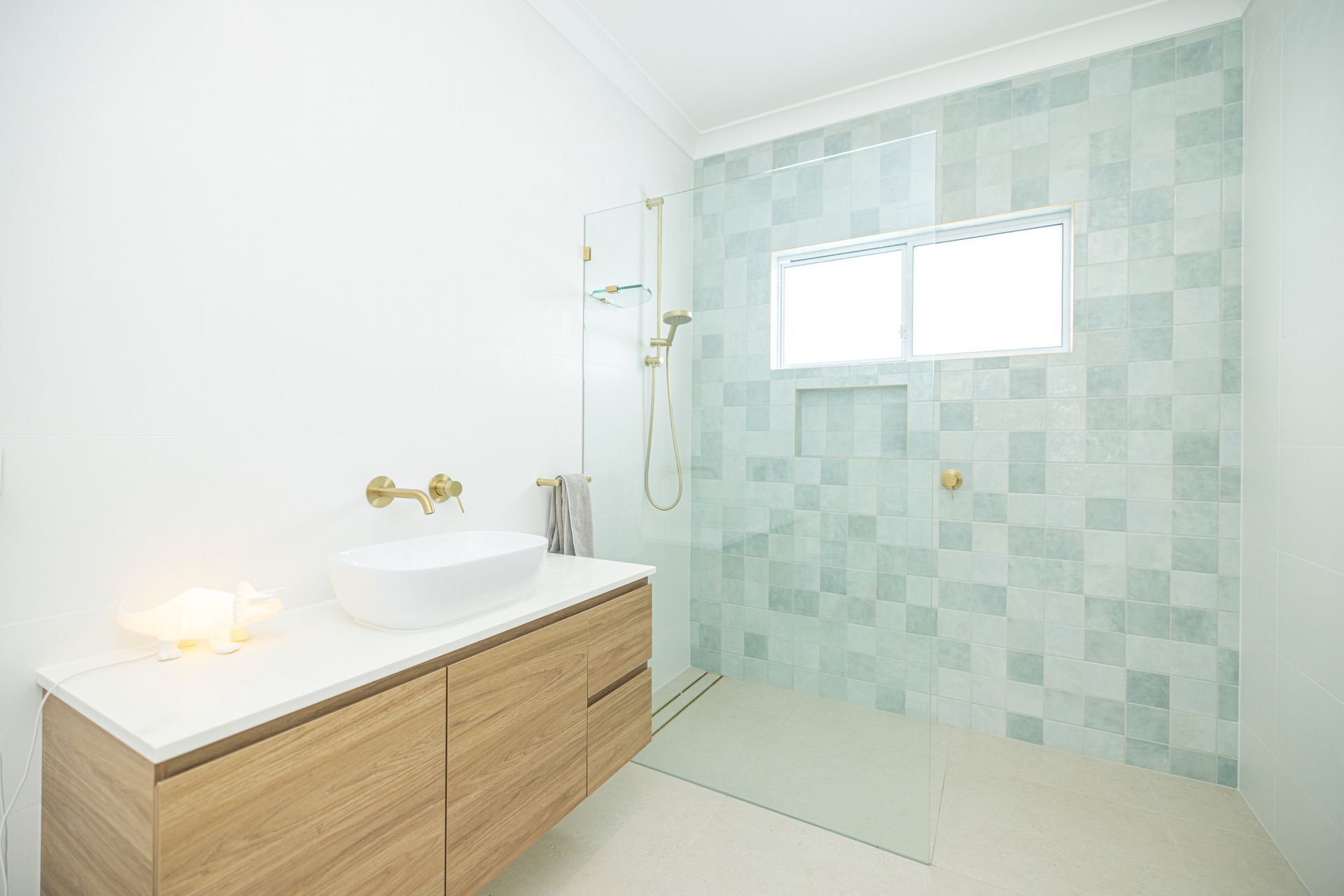 Modern bathroom with wood vanity, white sink, and glass shower with blue-green tile. — Blue Horizon Projects in Bateau Bay, NSW