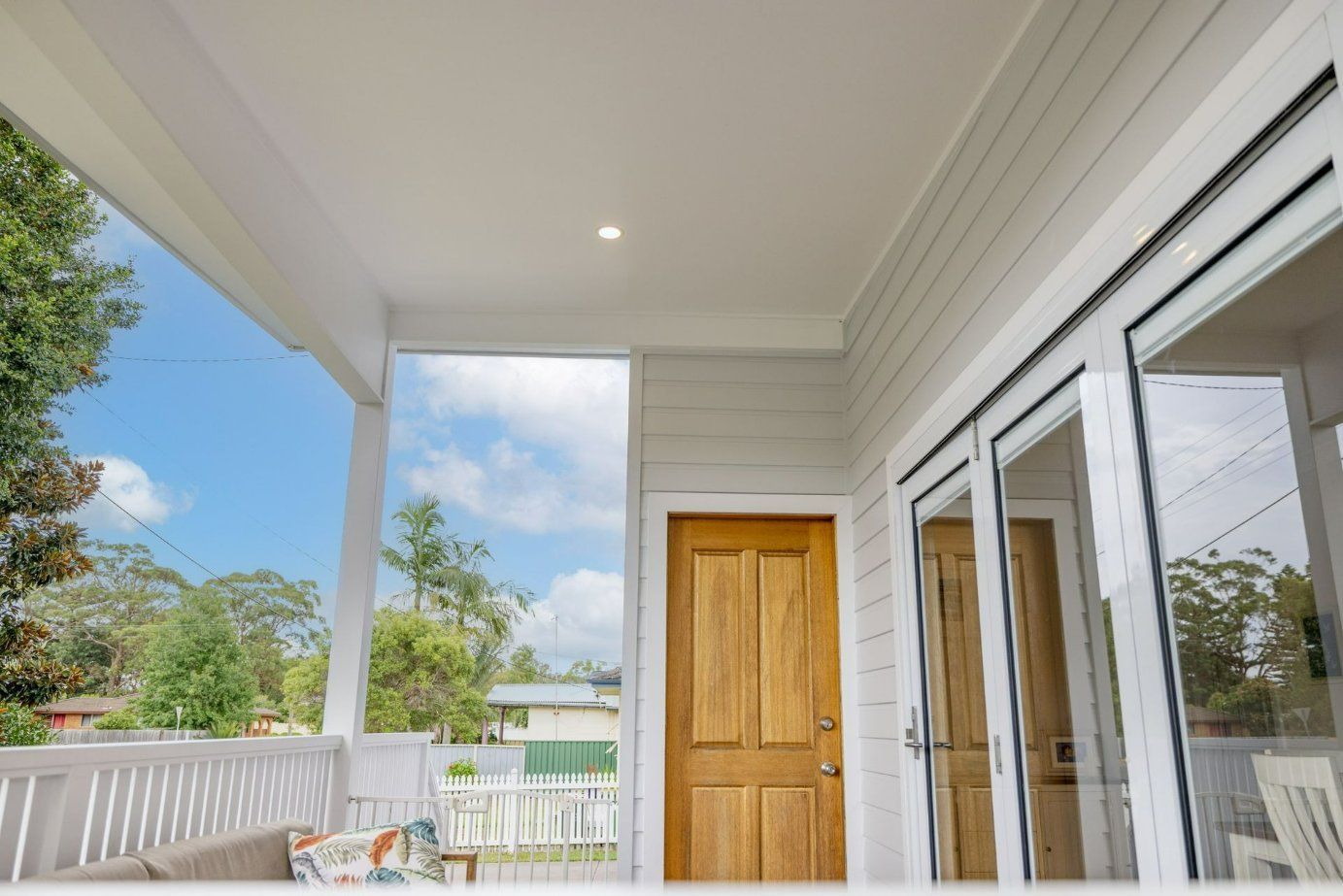 Wooden door and sliding glass doors on a covered porch with white trim, overlooking a yard. — Blue Horizon Projects in Bateau Bay, NSW