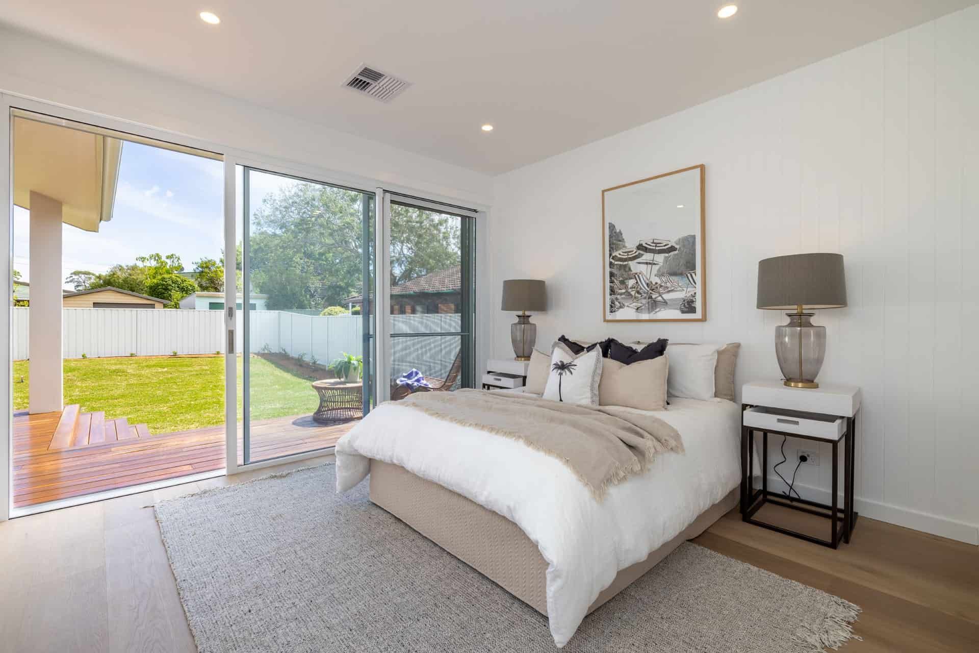 A Bedroom with A Large Bed and A Sliding Glass Door Leading to A Backyard — Blue Horizon Projects in Bateau Bay, NSW