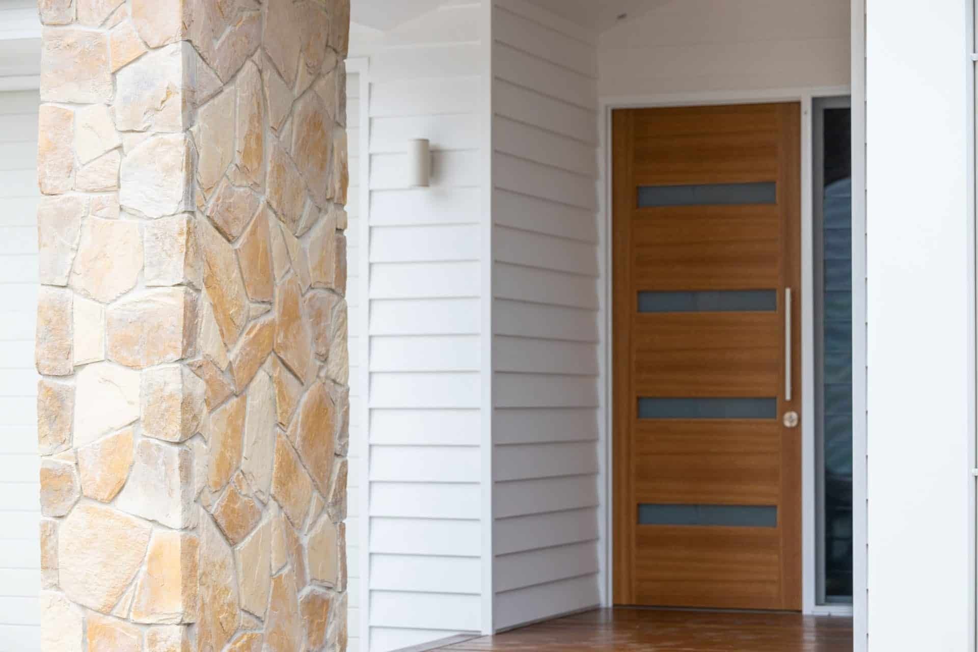 The Front Door of A House with A Stone Wall and A Wooden Door — Blue Horizon Projects in Bateau Bay, NSW