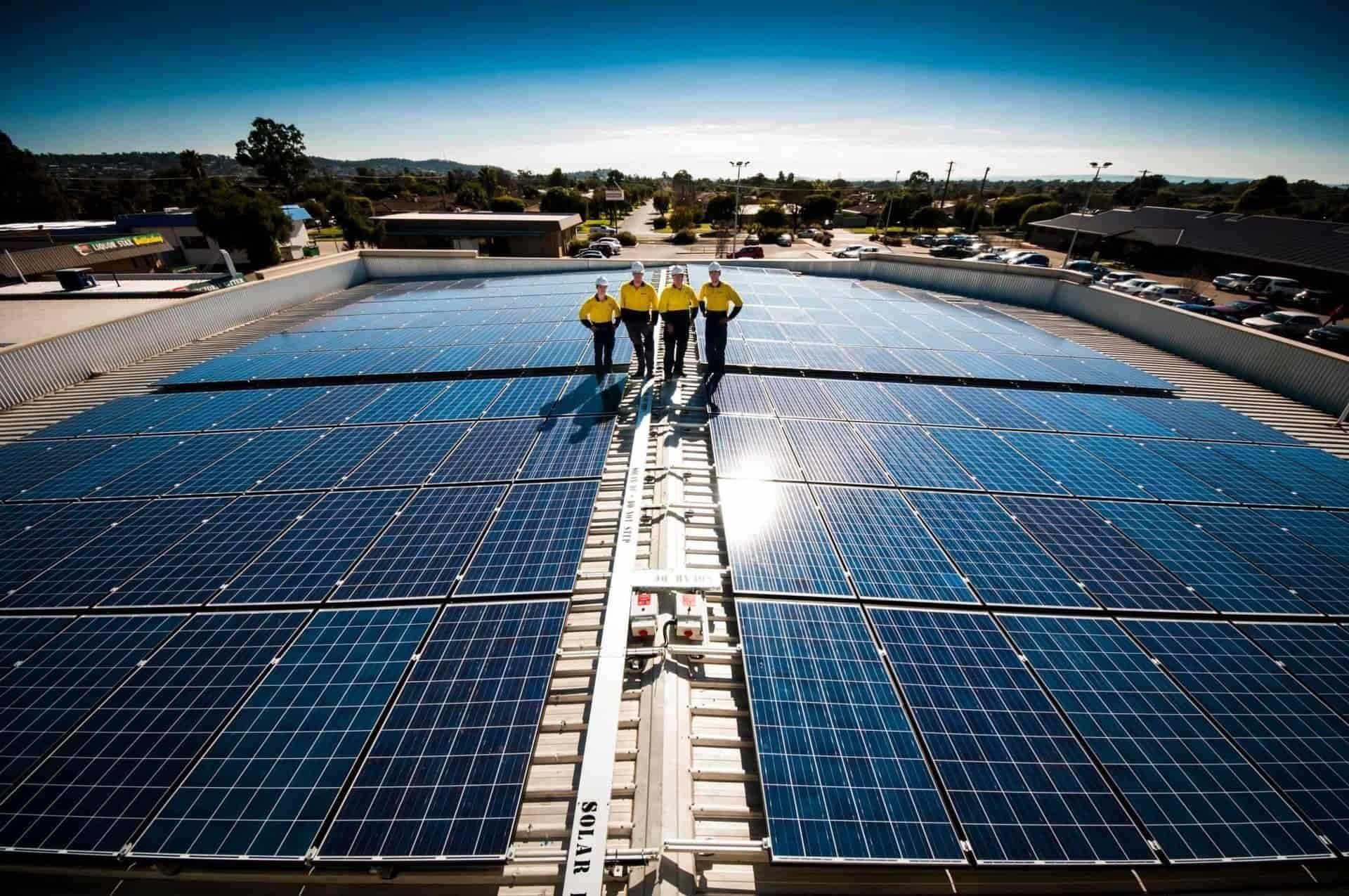 A Group Of Workers Standing On Top Of A Roof With Solar Panels — Des Mullins Electrical in Kooringal, NSW