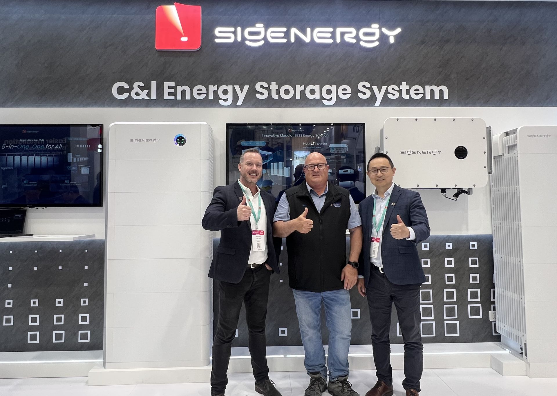 Three men are standing in front of a sign that says C & I energy storage system — Des Mullins Electrical in Kooringal, NSW