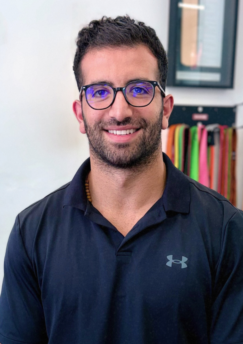 Man wearing glasses smiles, in a dark shirt, in an interior setting.