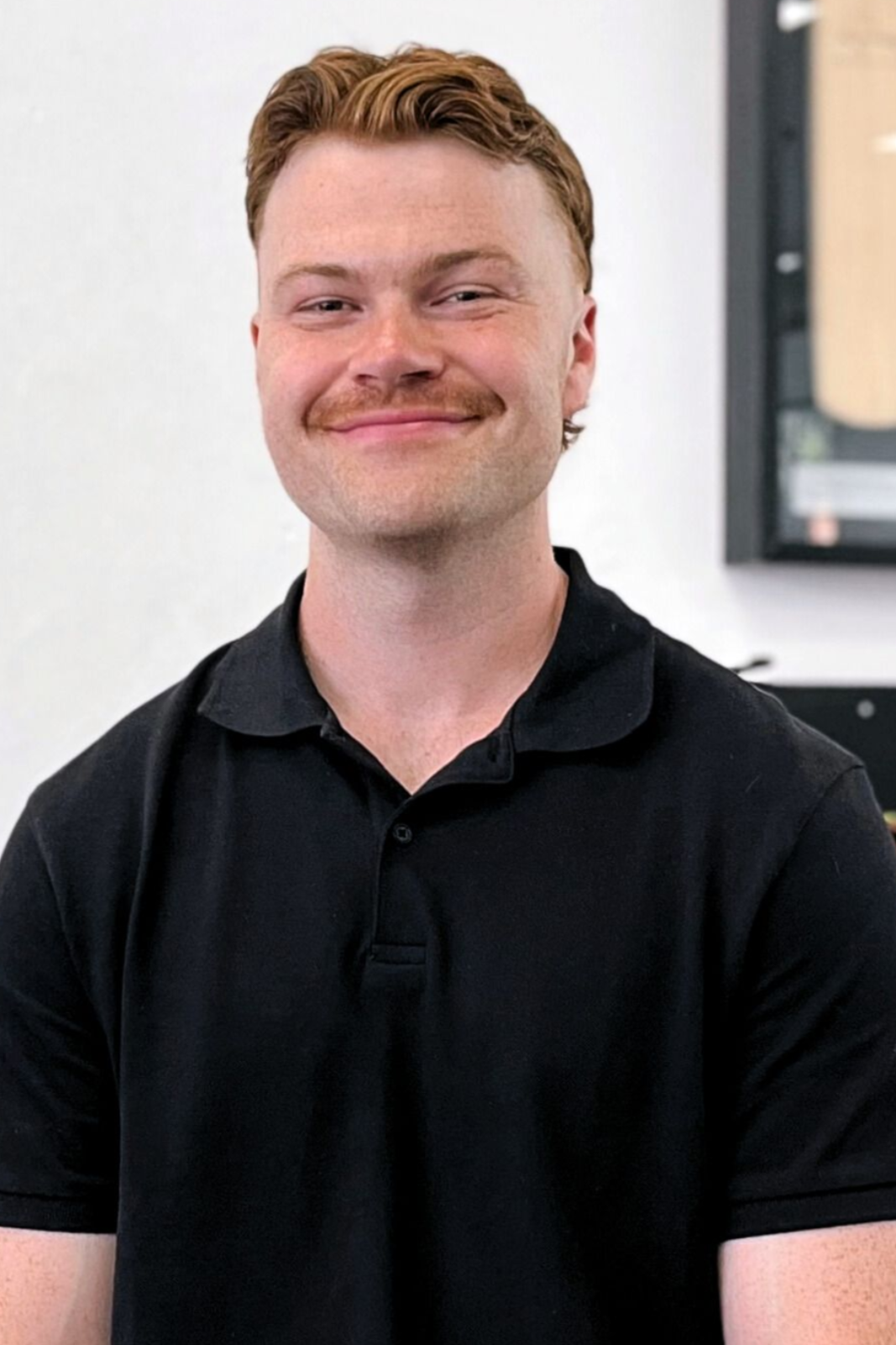Man with red hair and mustache wearing a blue shirt smiles, standing by colorful ribbons.