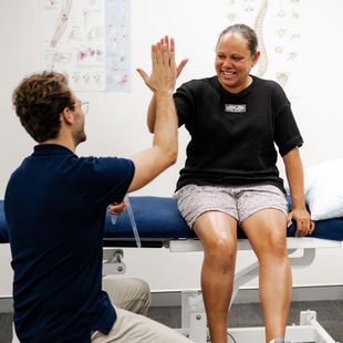 Man and woman high-fiving. They are in a medical exam room. The woman is seated on a bed.