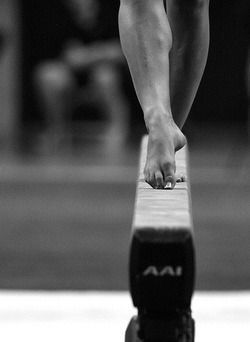 Gymnast's bare foot on balance beam, monochrome shot in a gymnasium.