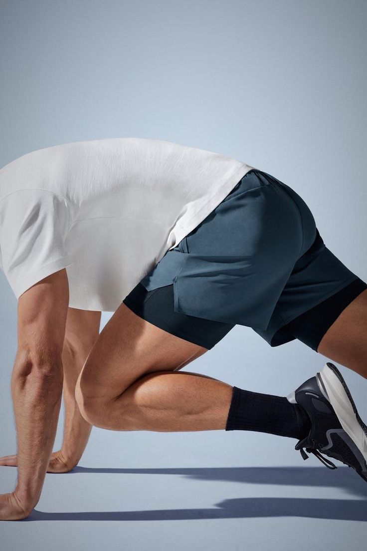 Runner in white shirt and blue shorts doing a crouched start on a track.