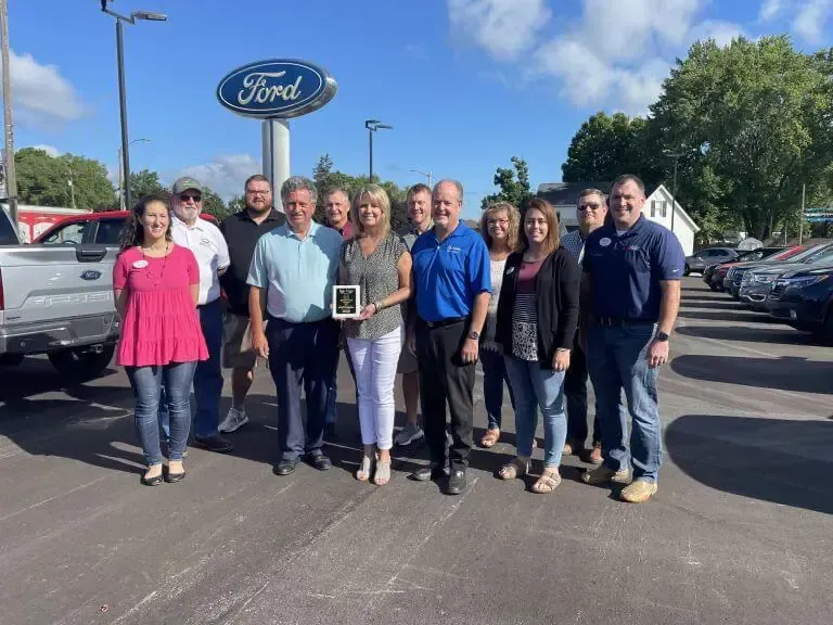 A group of people standing outside a Ford dealership, with one person holding a small award.