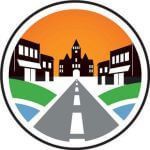 A stylized town logo featuring a central clock tower building, storefronts on either side, and a road leading toward them.