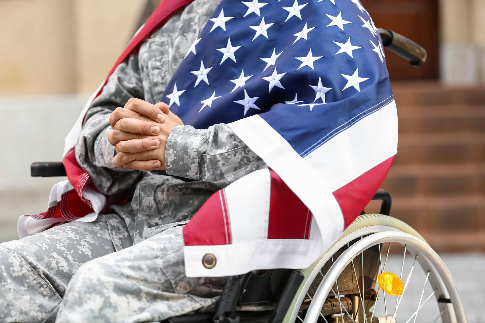 Person in a wheelchair wrapped in an American flag, hands clasped in front.