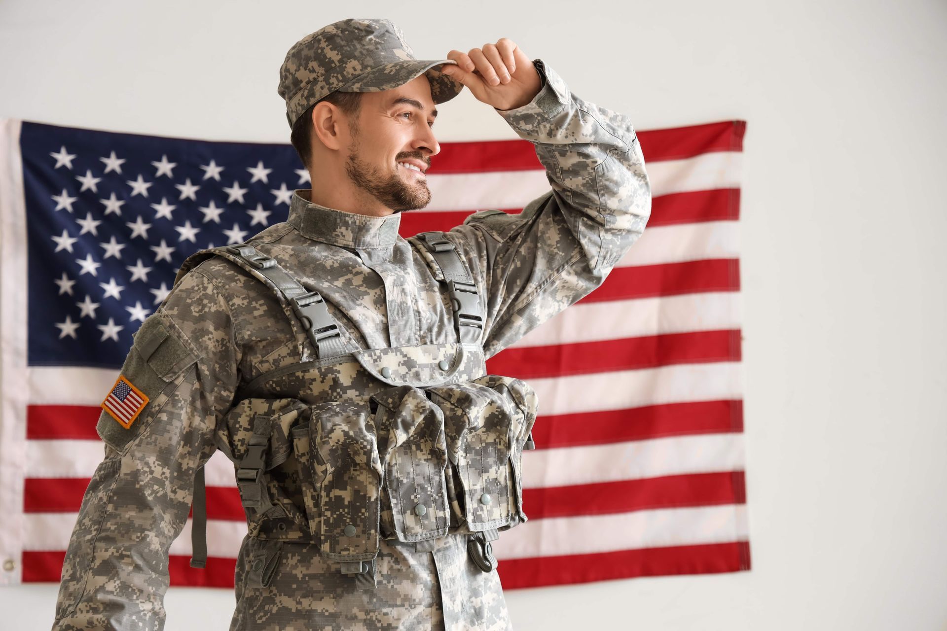 Soldier in camouflage saluting in front of a U.S. flag backdrop