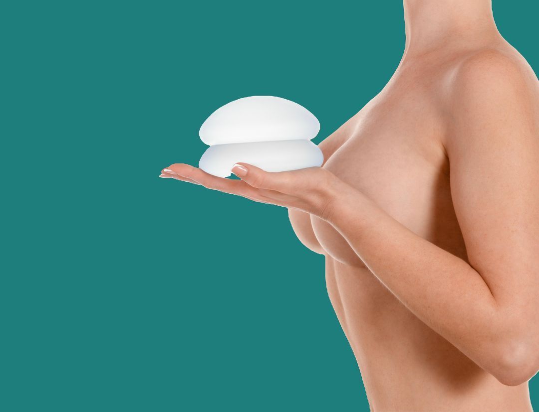Woman holding two breast implants next to her chest.