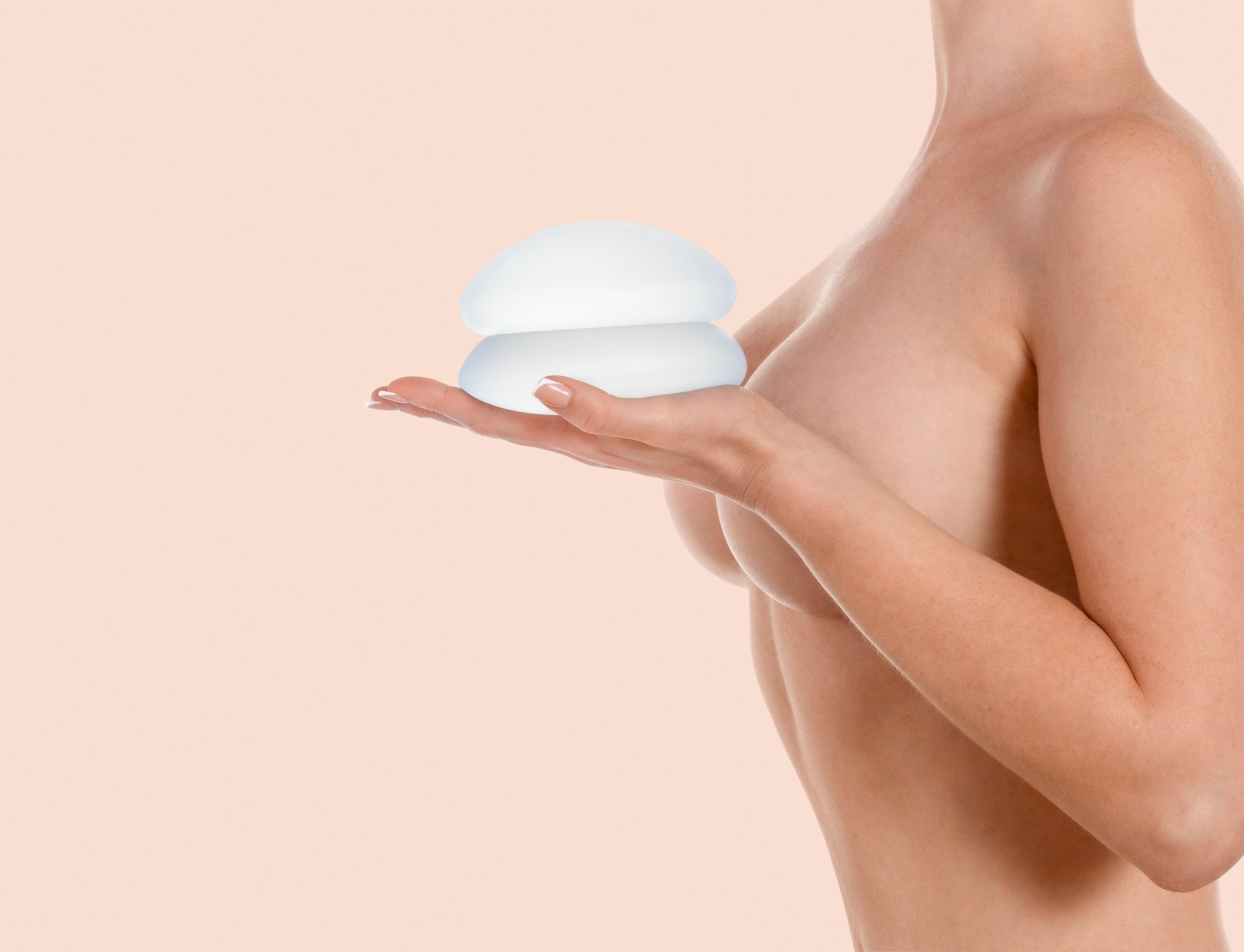 Woman holding two breast implants next to chest.