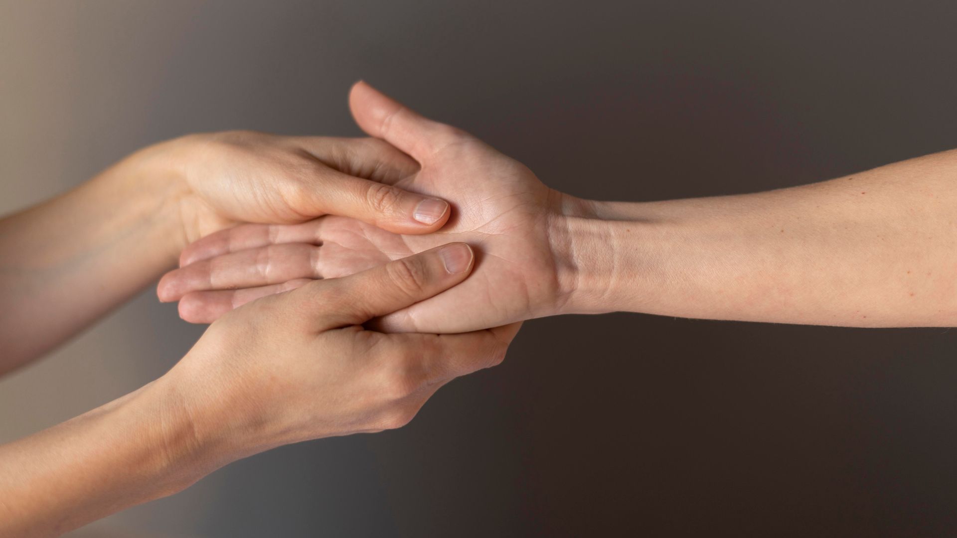 Hands receiving a hand massage, held by another person's hands. Gray background.