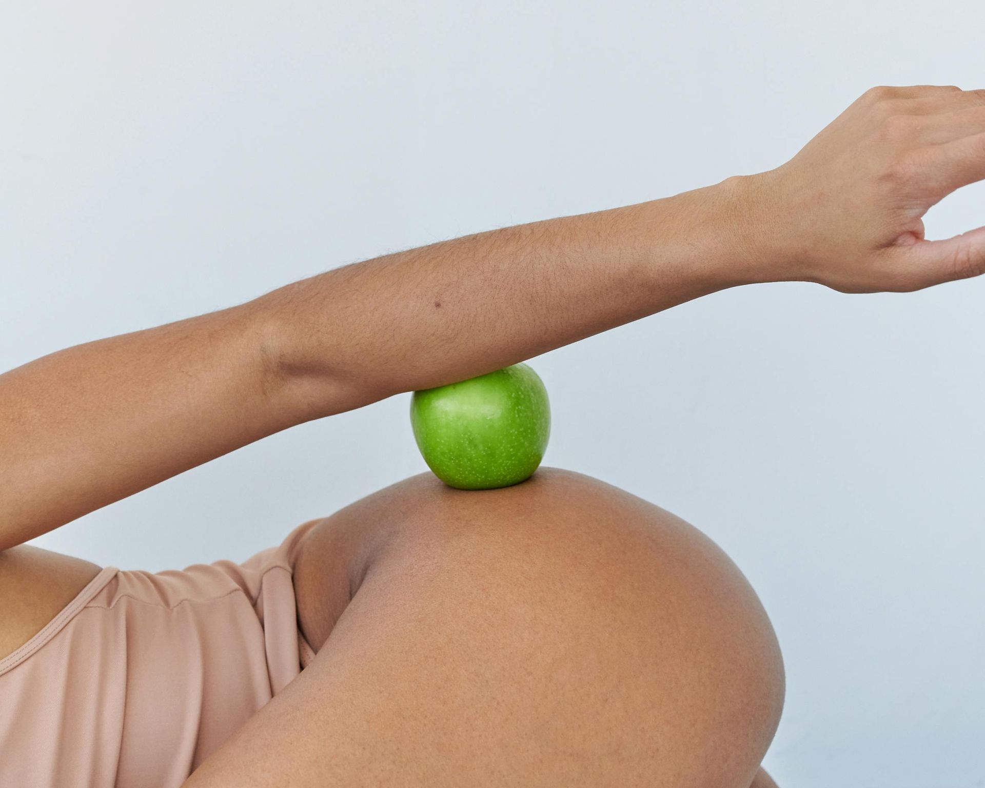 Arm balancing a green apple on a bent knee against a neutral backdrop.