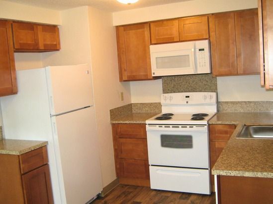 Kitchen with white appliances, wood cabinets, and speckled countertops.