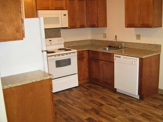 Kitchen with white appliances, brown cabinets, and wood-look flooring.
