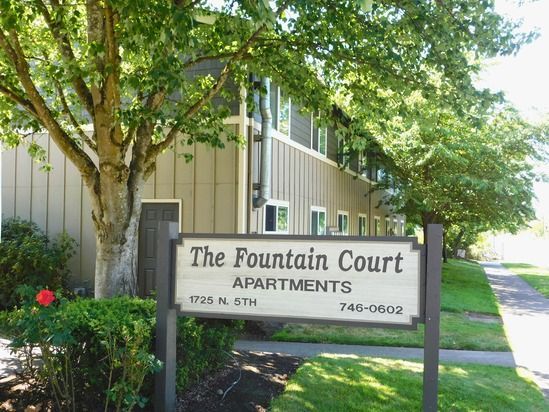 Sign for The Fountain Court Apartments, 1725 N. 6th, in front of a two-story apartment building, with trees and lawn.