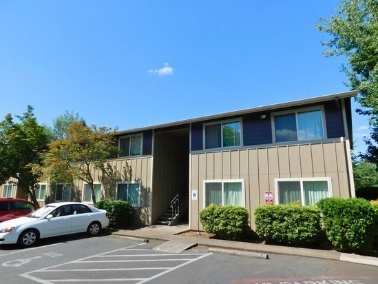 Apartment building with parking; a white car is parked on the left side under a clear blue sky.