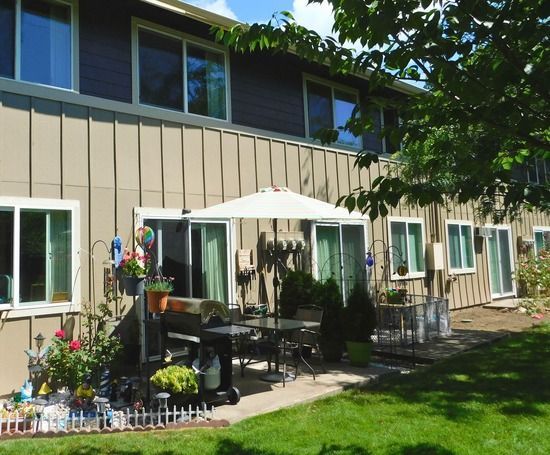 Row of townhouses with a patio featuring an umbrella, table, grill, and garden on the green lawn.