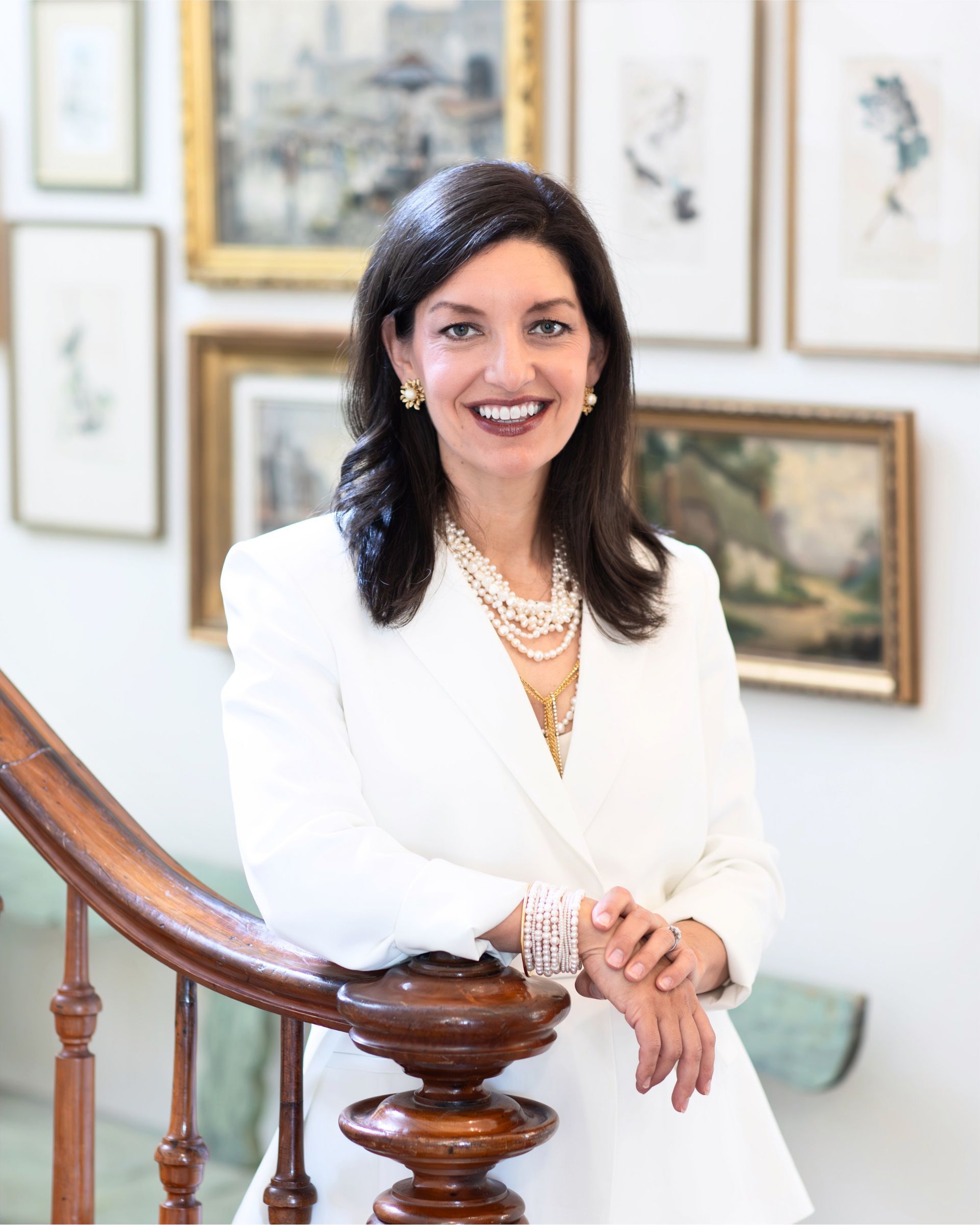 A portrait of Kimberly wearing a white shirt and a pearl necklace is smiling for the camera.