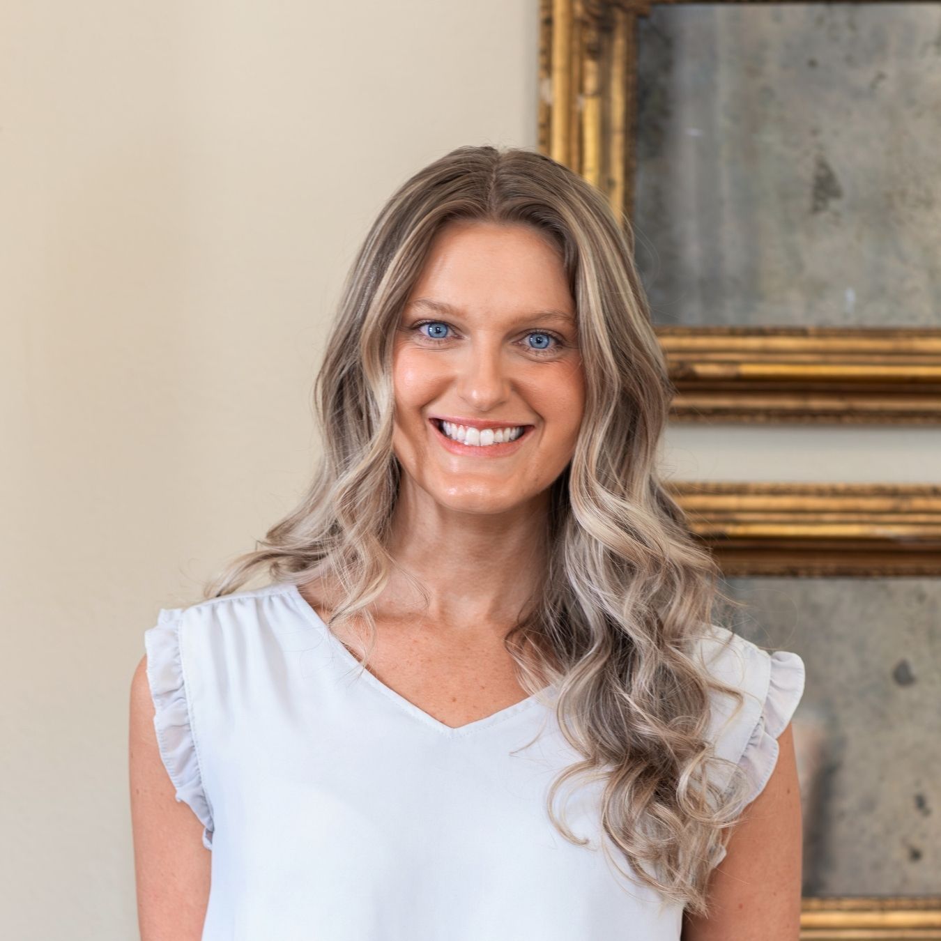 A portrait of Lexi wearing a beige shirt with curled hair smiling for the camera.
