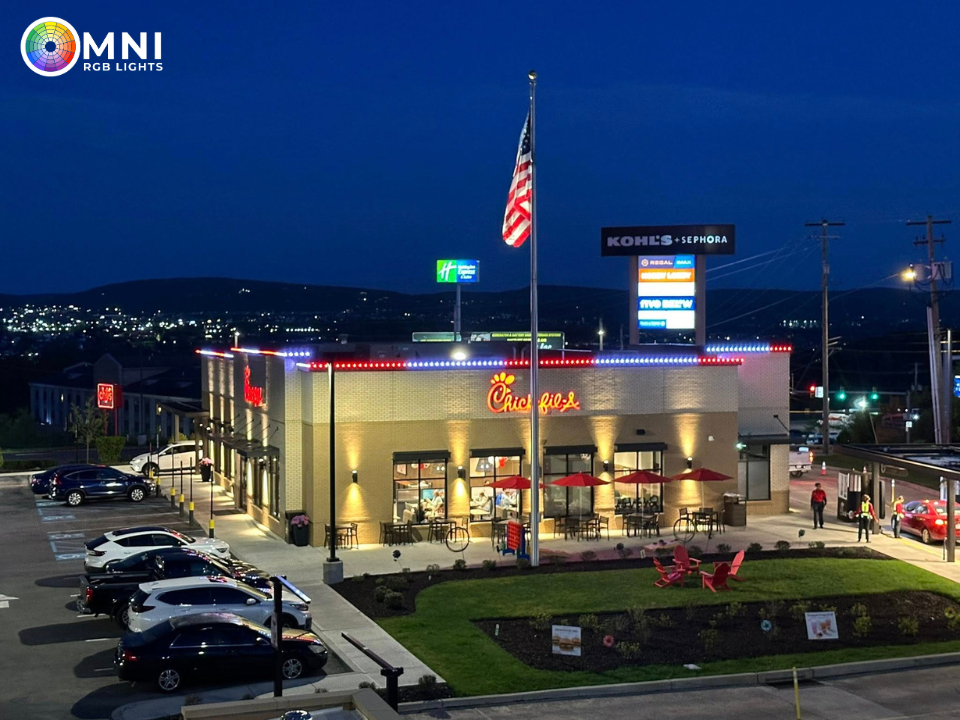 Nighttime aerial view of a Chick-fil-A restaurant with a lit parking lot and U.S. flag, next to an OMNI sign