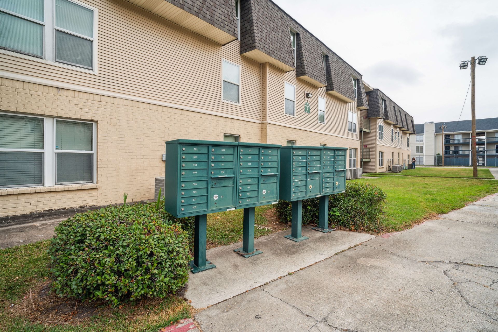 Row of green mailboxes outside beige apartment buildings along a sidewalk
