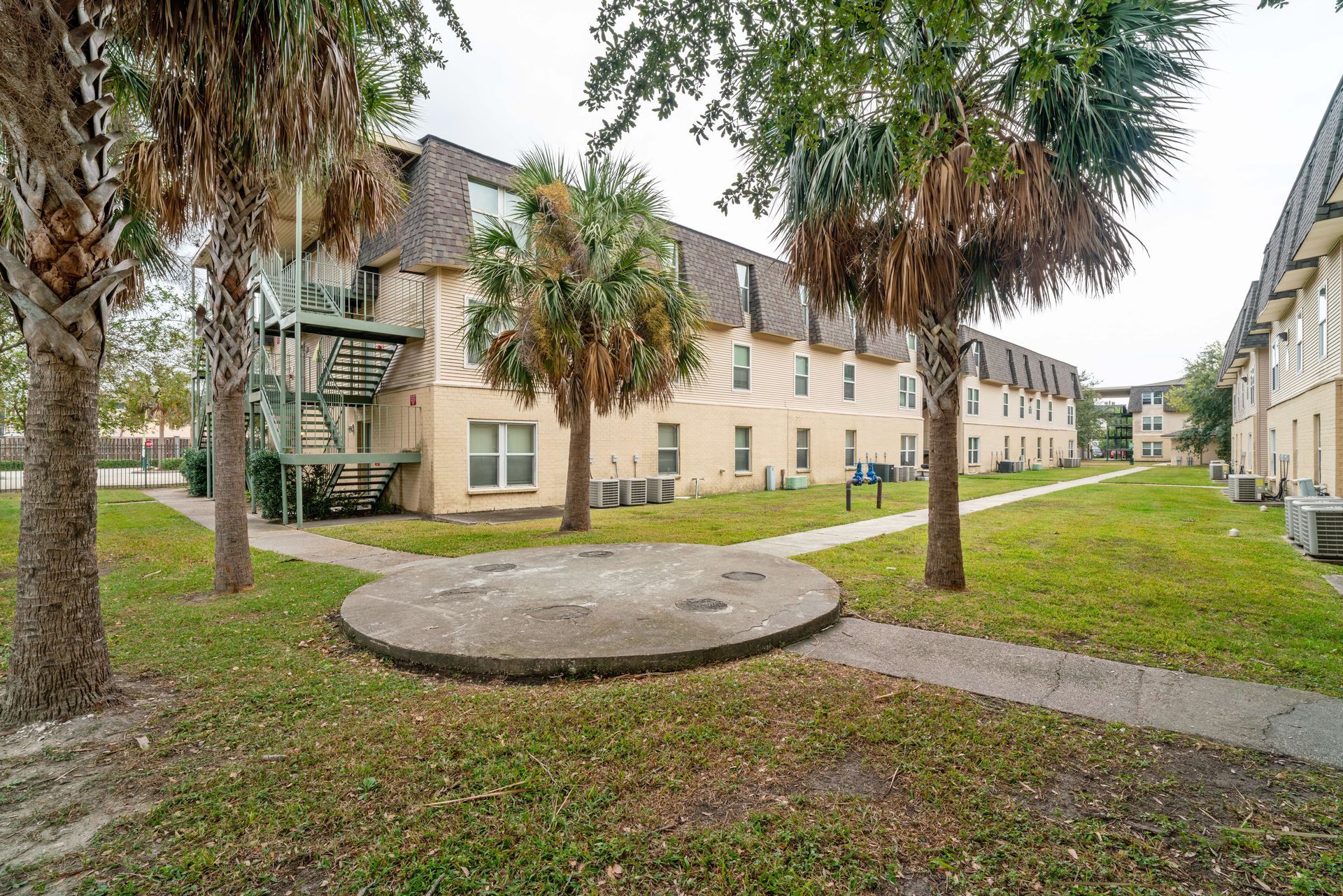 Courtyard of beige apartment buildings with palm trees, grass, and a circular concrete platform