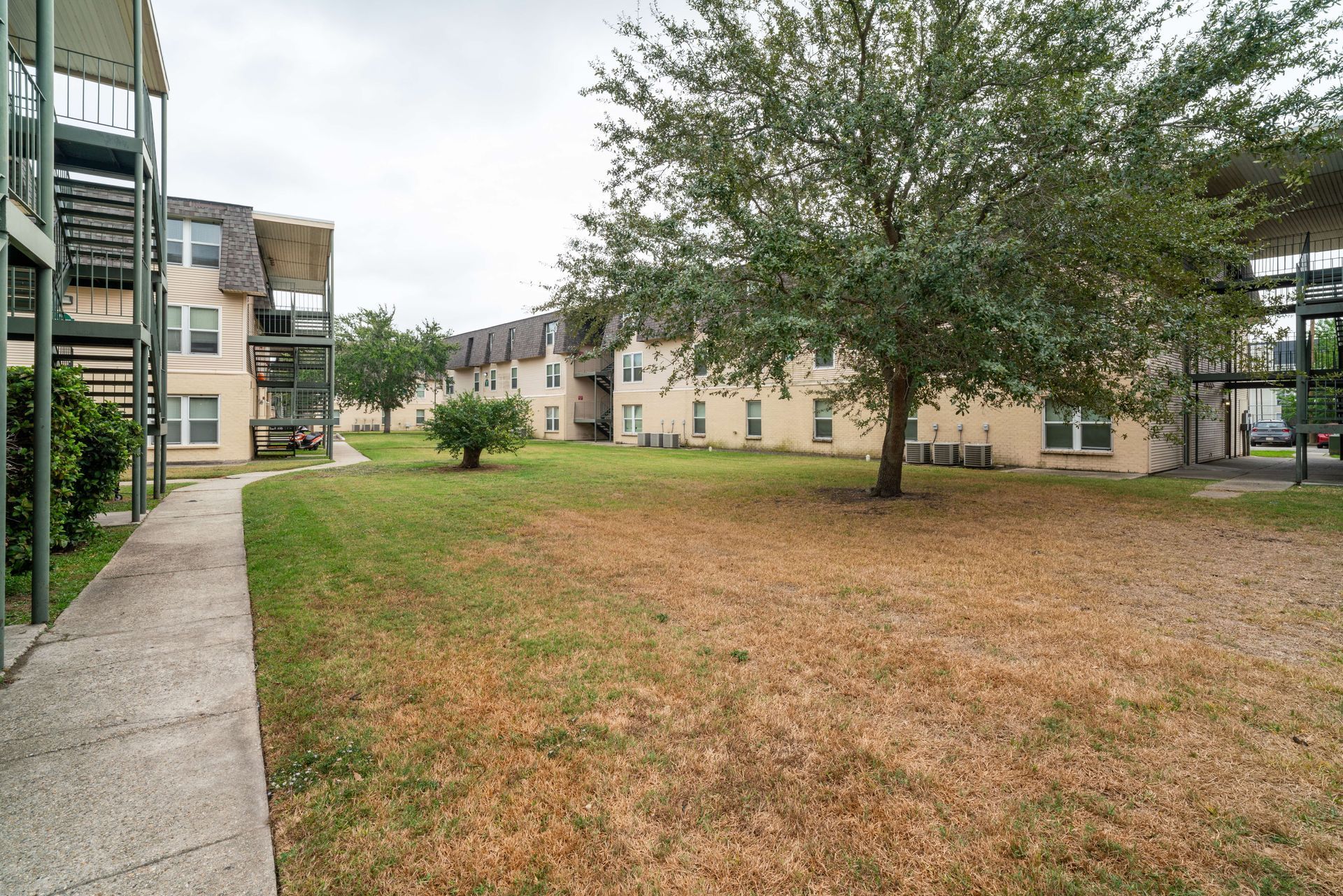 Apartment courtyard with trees, grass, and walkways beside beige buildings