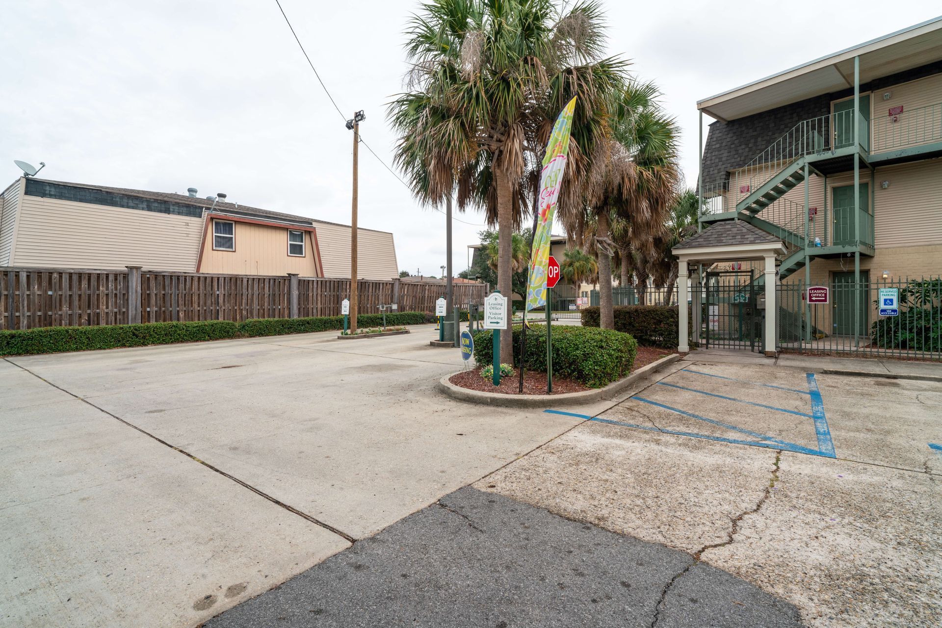 Apartment parking lot with palm trees, cracked pavement, and building entrance under overcast sky
