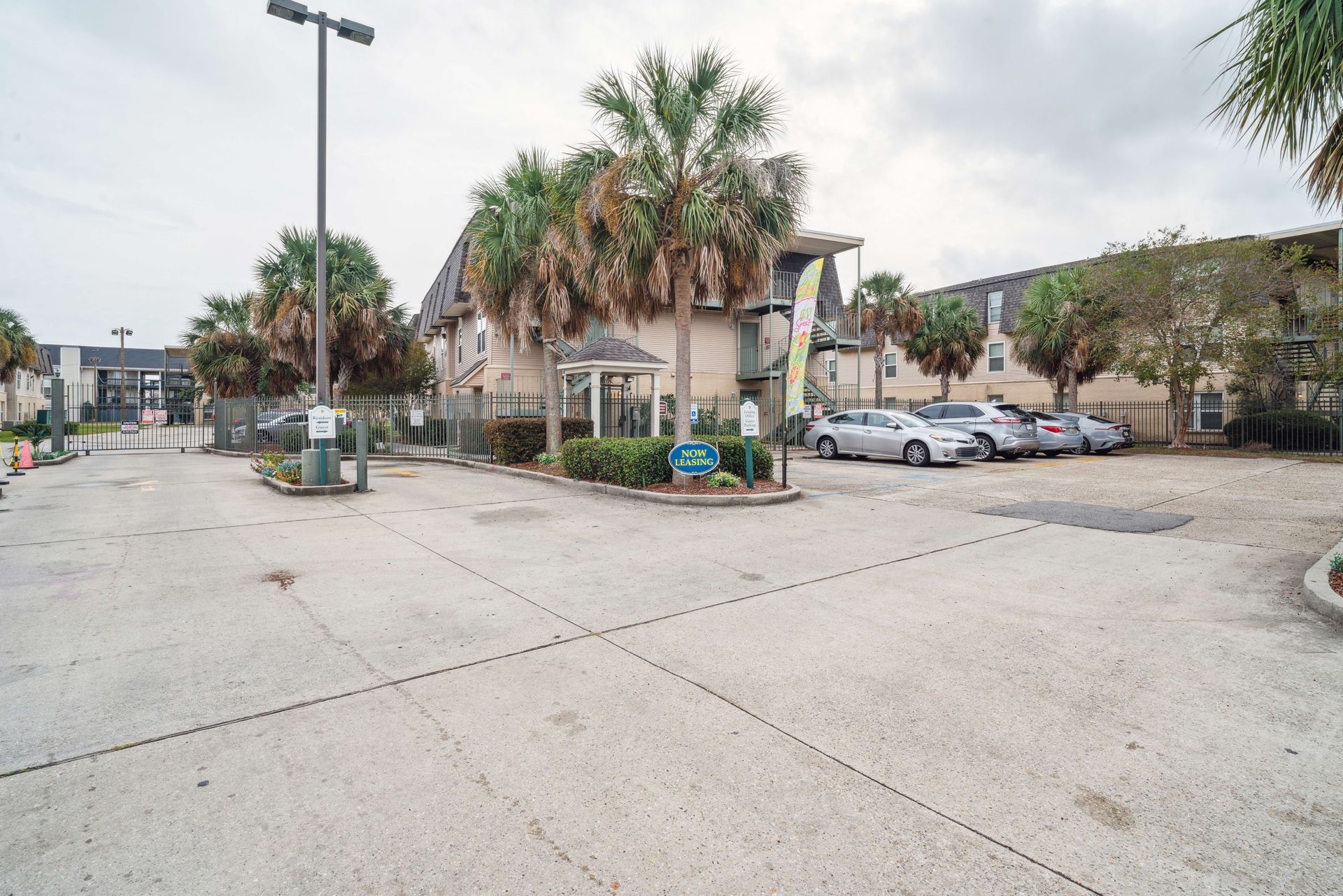Parking lot with palm trees, apartment buildings, and several parked cars on a cloudy day