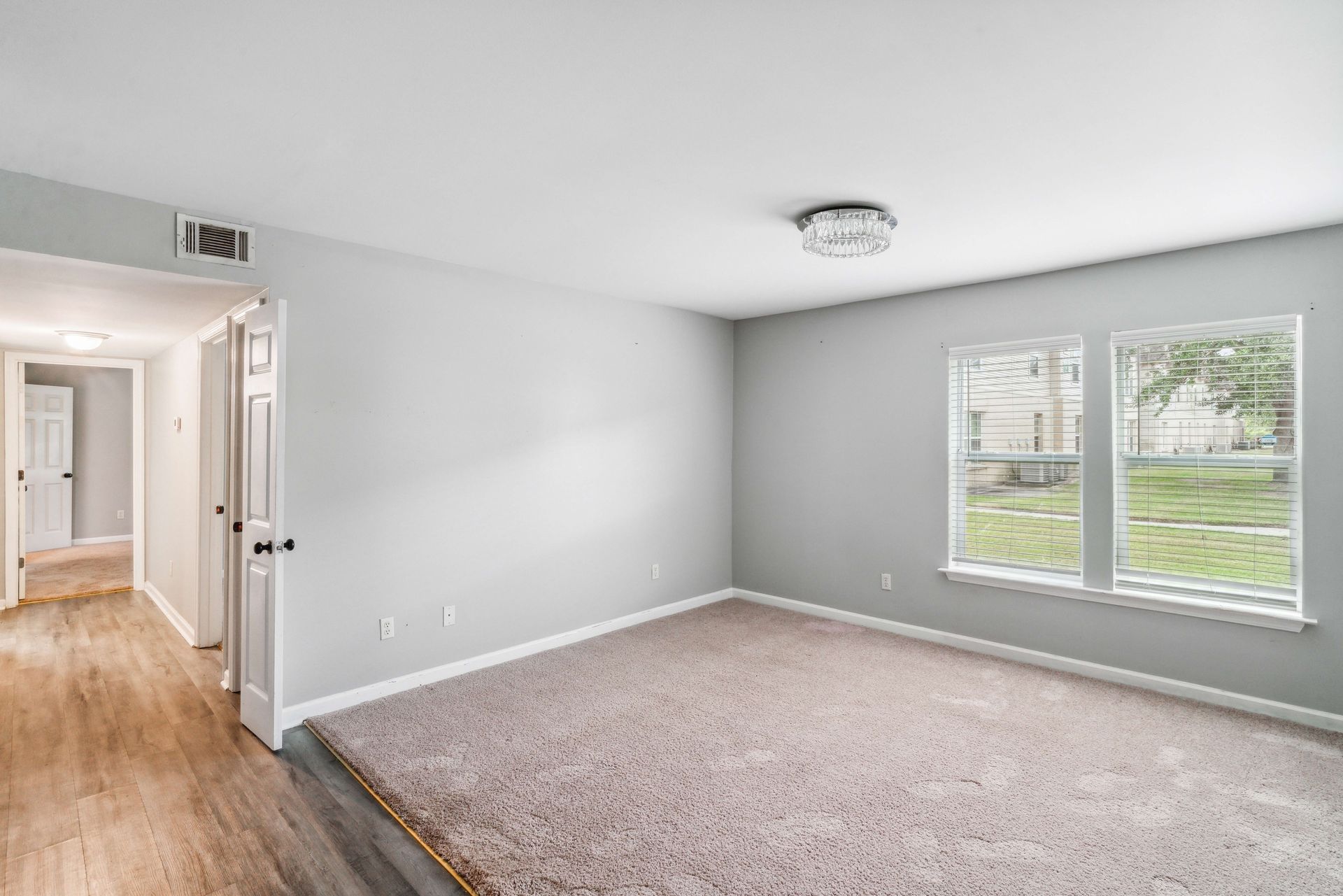 Empty carpeted living room with gray walls, white trim, and a large window