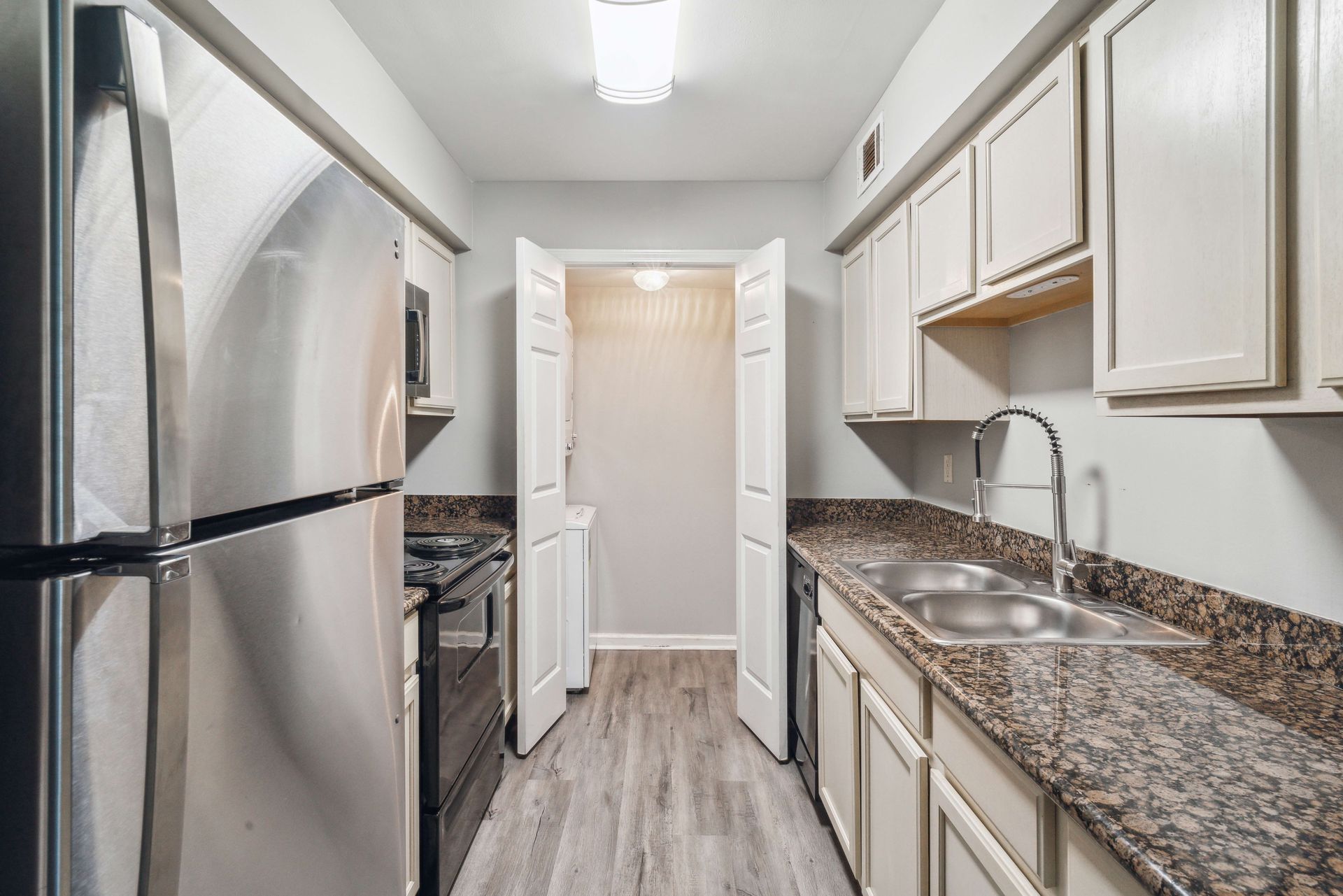 Narrow kitchen with stainless steel fridge, white cabinets, granite counters, and wood-look floor