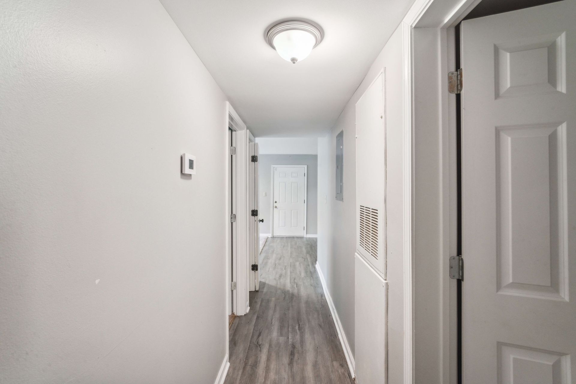 Bright white hallway with gray wood floors, doors on both sides, and a ceiling light.