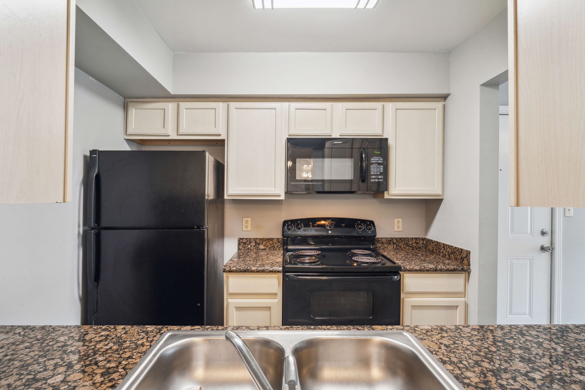 Small kitchen with black appliances, white cabinets, and a double sink in the foreground